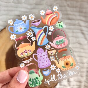 May include: A clear sticker sheet with colorful teapots, cups, and flowers. The text "spill the tea" is written in cursive at the bottom of the sheet.