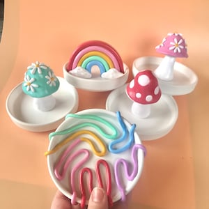 Puede incluir: Conjunto de cuatro platos de anillo de cer&aacute;mica con decoraciones de arcilla de colores. Los platos presentan un arco&iacute;ris, un hongo con puntos blancos, un hongo con flores blancas y un remolino de arcilla de colores.