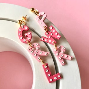 May include: Pink and white polka dot letter earrings spelling out "GIRL".