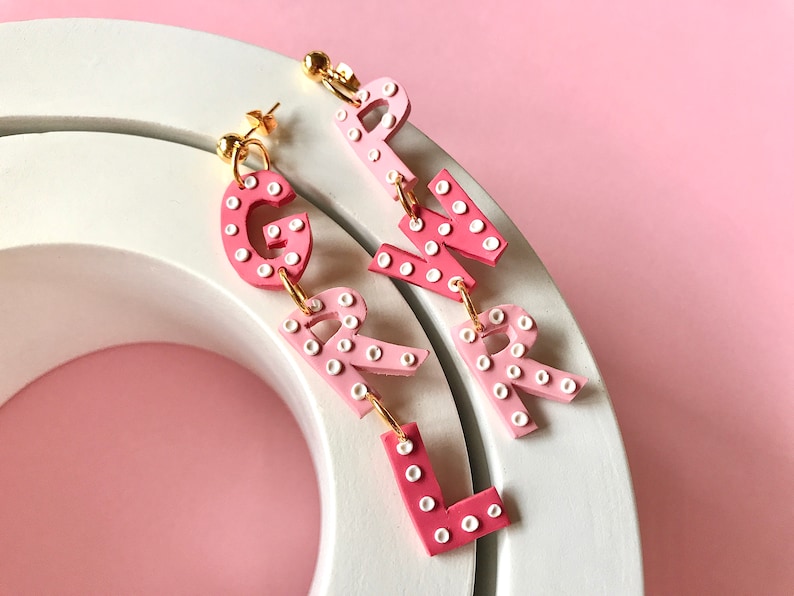 May include: Pink and white polka dot letter earrings spelling out "GIRL".