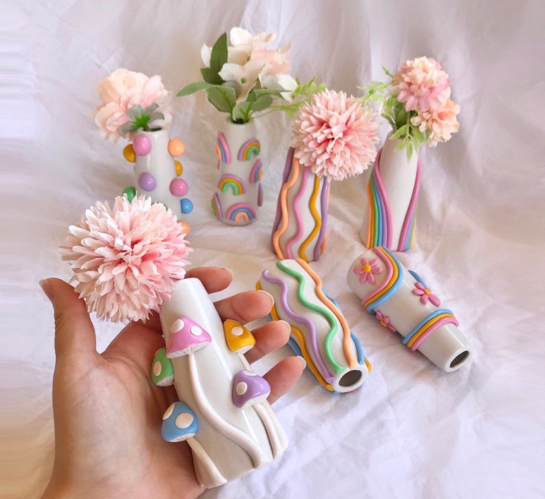 May include: A set of seven colorful ceramic vases with rainbow designs. The vases are decorated with flowers and are arranged on a white surface.