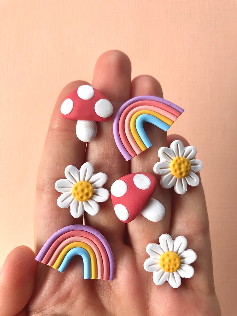 May include: A set of six colorful clay earrings featuring a rainbow, mushroom, and daisy designs. The earrings are handmade and have a whimsical, retro aesthetic.
