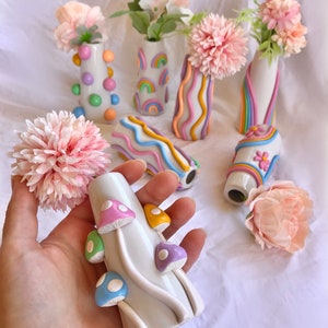 May include: Set of six ceramic vases with various colorful designs. The vases are decorated with rainbows, wavy lines, and polka dots. One vase features a mushroom design with pastel-colored mushrooms.