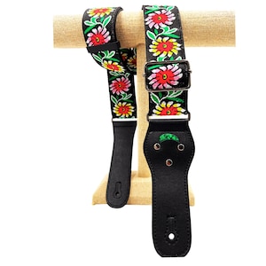 May include: Black guitar strap with a floral pattern in red, yellow, green, and pink. The strap has a black leather end with a metal buckle.