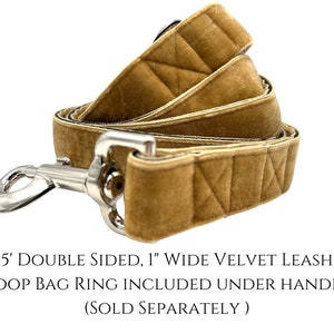K&ouml;nnte beinhalten: Eine 1,5 Meter lange, doppelseitige, 2,5 cm breite Hundeleine aus Samt in hellbrauner Farbe. Die Leine hat ein gestepptes Muster und einen silbernen Clip. Der Text "5' DOUBLE SIDED, 1" WIDE VELVET LEASH POOP BAG RING INCLUDED UNDER HANDLE (SOLD SEPARATELY)" ist unter der Leine gedruckt.