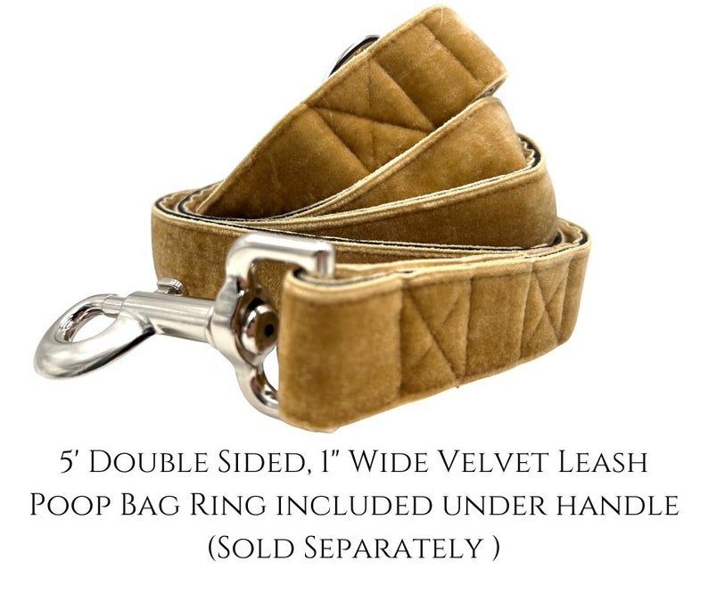 K&ouml;nnte beinhalten: Eine 1,5 Meter lange, doppelseitige, 2,5 cm breite Hundeleine aus Samt in hellbrauner Farbe. Die Leine hat ein gestepptes Muster und einen silbernen Clip. Der Text "5' DOUBLE SIDED, 1" WIDE VELVET LEASH POOP BAG RING INCLUDED UNDER HANDLE (SOLD SEPARATELY)" ist unter der Leine gedruckt.