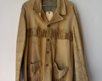 Peut inclure: Une veste en cuir beige avec de longues franges sur la poitrine, les poches et l'ourlet. La veste présente un col classique, une fermeture boutonnée sur le devant et deux poches. Une étiquette en papier beige est suspendue au col.