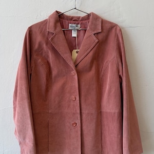 May include: A dusty rose suede blazer featuring a notched lapel, long sleeves, and a three-button front closure. The garment includes a Pendleton brand label at the inner neckline and a small beige paper tag attached to the collar area.