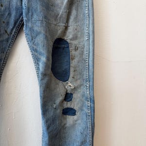 K&ouml;nnte beinhalten: Hellblaue Jeans mit Distressed-Details, einschlie&szlig;lich eines gro&szlig;en Knierisses und Flicken. Die Jeans weisen Gebrauchsspuren auf, mit sichtbarem Ausbleichen und Flecken, was ihnen einen Vintage-Look verleiht. Klassische Jeans im Five-Pocket-Stil.
