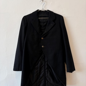 May include: A black tailcoat jacket featuring a notched lapel, two metallic buttons on the front closure, and a long, split-tail design. The garment is constructed with a smooth, solid black fabric and includes a structured collar and long sleeves.