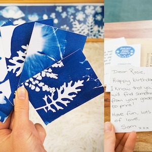 May include: A set of five cyanotype prints featuring white leaf silhouettes on a blue background. The prints are held in a hand and are accompanied by a handwritten note that reads "Dear Rosie, Happy birthday I know that you will find something from your garden to print! Have fun, lots of love, Sam xxx".