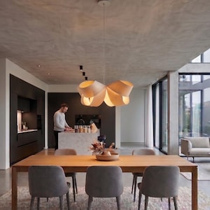 Puede incluir: Una lámpara colgante de madera de color claro con un diseño escultural en forma de cinta suspendida del techo. La lámpara presenta múltiples bucles curvos y superpuestos de chapa de madera fina que emiten un brillo cálido y suave.