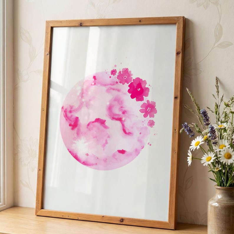 May include: A framed wall art print featuring a large, circular watercolour painting in shades of pink. The centre of the circle has a marbled, cloud-like texture, while the upper right edge is decorated with several small, vibrant pink flowers.