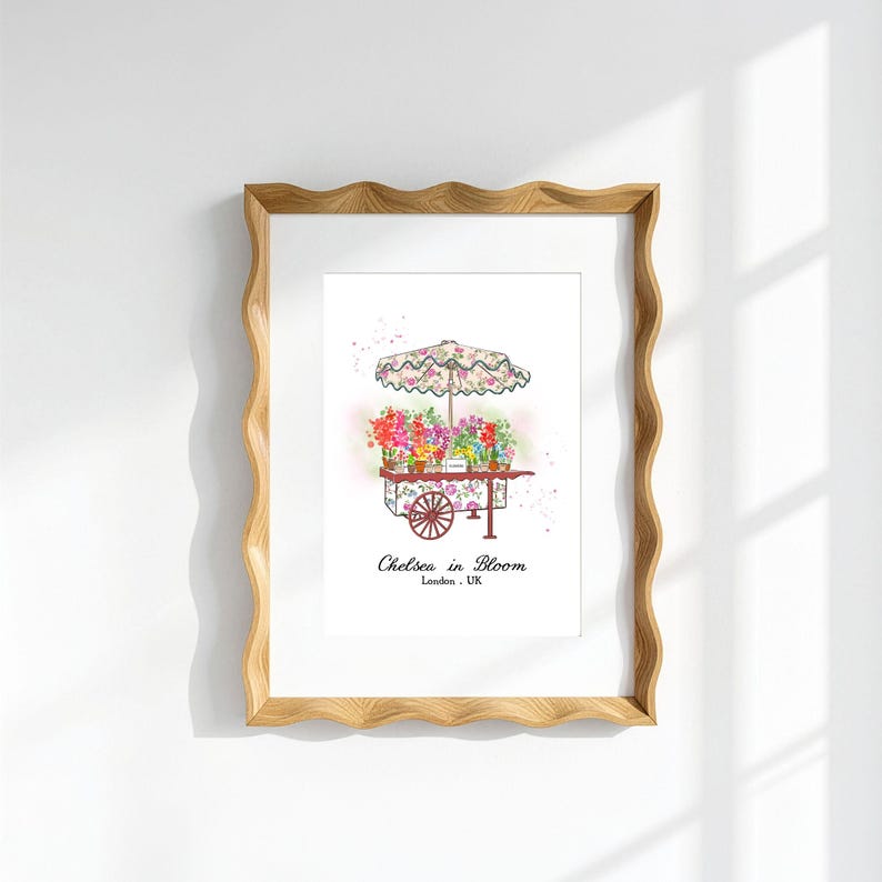 K&ouml;nnte beinhalten: Ein gerahmter Kunstdruck mit einer Aquarellillustration eines Blumenwagens mit einem blumig gemusterten Sonnenschirm. Der Wagen ist mit bunten Blumen gef&uuml;llt und zeigt unterhalb den Text Chelsea in Bloom London, UK in einer schwarzen Serifenschrift.