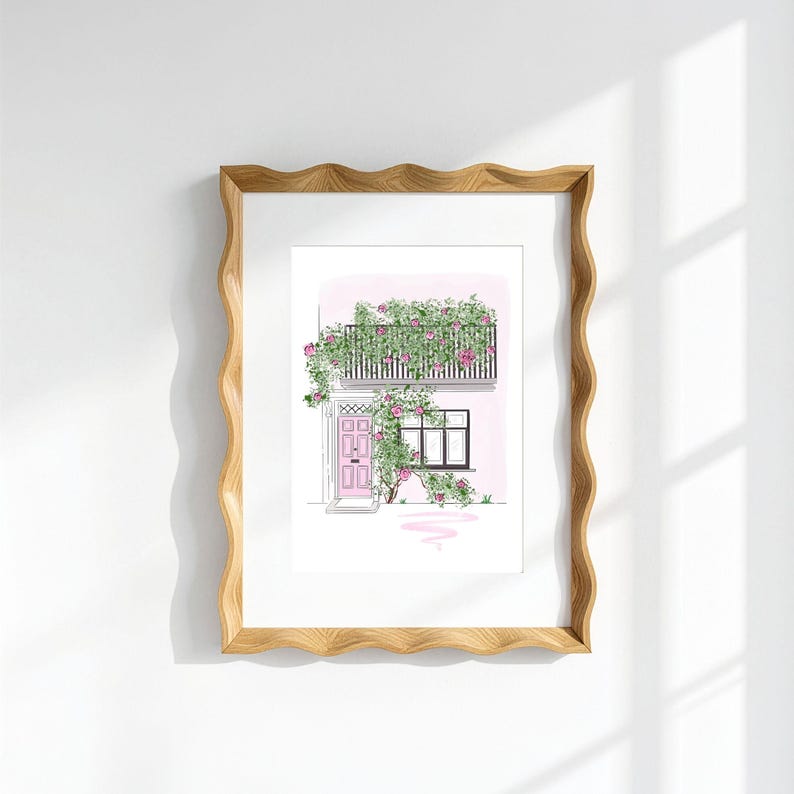May include: A framed art print featuring a line drawing of a building facade with a pink door and a balcony covered in climbing pink roses and green leaves. The frame has a wavy, light brown wooden edge and a white mat border around the print.