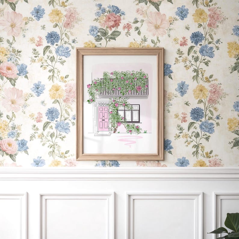 May include: A framed art print featuring a watercolor illustration of a building facade with a pink door, a black balcony, and climbing green vines with pink flowers. The artwork is displayed against a floral wallpaper background with blue, yellow, and pink blossoms.