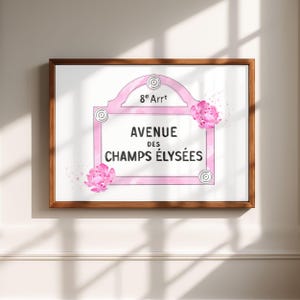 Może przedstawiać: Oprawiony wydruk z r&oacute;żowym wzorem znaku ulicznego z napisem "AVENUE DES CHAMPS &Eacute;LYS&Eacute;ES" i "8e Arr". Akwarelowe r&oacute;żowe kwiaty zdobią projekt. Rama ma ciepły brązowy kolor.