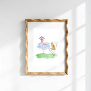 May include: A framed watercolor illustration featuring a ginger tabby cat sitting on a white metal chair next to a round table with a blue floral tablecloth. On the table sits a red and white striped pitcher with pink tulips and a small cup.