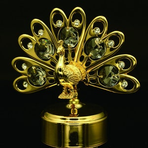 May include: A gold-tone musical jewelry box shaped like a peacock with crystal accents. The peacock's tail feathers are spread out and decorated with clear crystals.