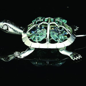 May include: A silver turtle figurine with a green crystal shell. The turtle is walking forward with its head raised.