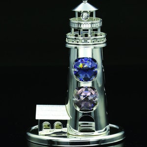 May include: Silver lighthouse figurine with three crystal accents: a clear crystal on top, a blue crystal in the middle, and a purple crystal at the bottom. The lighthouse is on a silver base.