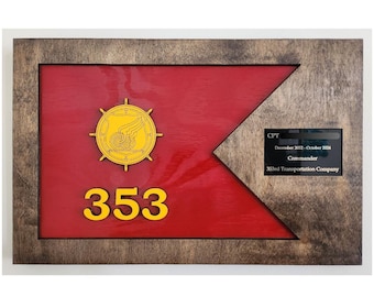 May include: A framed wooden plaque featuring a red flag design with a gold emblem and the number 353 in yellow. A black plaque with white text reads "CPT December 2022 - October 2024 Commander 353rd Transportation Company."