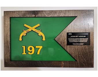 May include: Wooden plaque with a green flag design, featuring crossed yellow pistols and the number 197. Includes text: "SSG AUGUST 2022-AUGUST 2023 FOR OUTSTANDING PERFORMANCE WHILE SERVING AS THE MILITARY POLICE INVESTIGATIONS NCOIC *PEACEMAKERS"