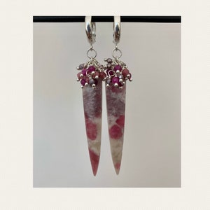 Può includere: Un paio di orecchini a cerchio d'argento con gocce di pietra rosa e bianca e perline rosa e argentate che pendono dalla parte inferiore.