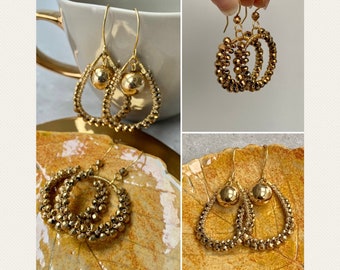 May include: Gold tone earrings with a teardrop shape and a small ball at the bottom. The earrings are made of small beads.