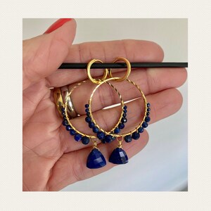 May include: Gold hoop earrings with a dangling lapis lazuli stone. The hoops are adorned with small lapis lazuli beads.
