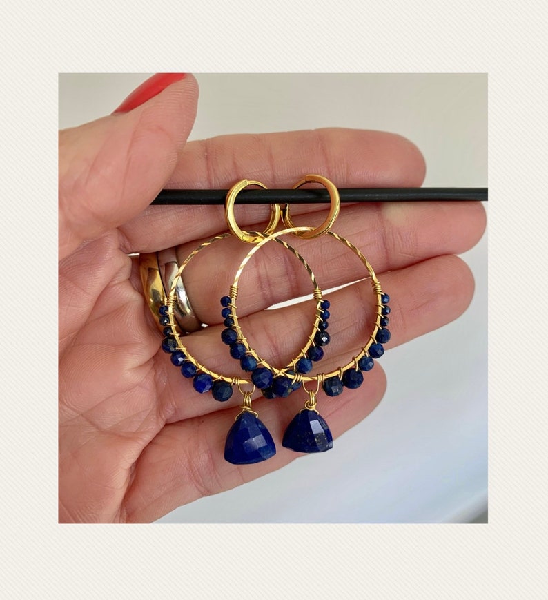 May include: Gold hoop earrings with a dangling lapis lazuli stone. The hoops are adorned with small lapis lazuli beads.