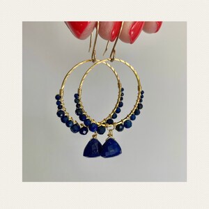 May include: Gold hoop earrings with a row of dark blue lapis lazuli beads and a dangling lapis lazuli gemstone.