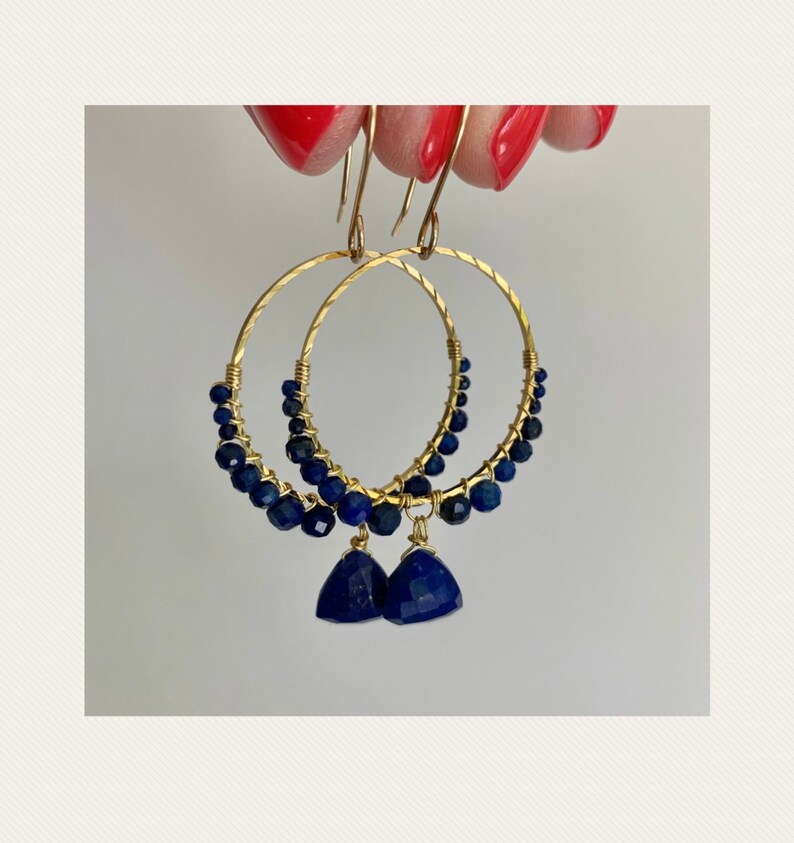 May include: Gold hoop earrings with a row of dark blue lapis lazuli beads and a dangling lapis lazuli gemstone.