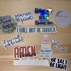 May include: A collection of colorful stickers with inspirational messages, including "You are beyond", "Shine on sister! Shine on", "I will not be shaken", "Let your results speak the loudest", "Amen & amen", "Excellence lives in the details", "Love, joy, peace, patience, kindness, goodness, faithfulness, gentleness, self-control", "Salt + Light", "Be salt be light", and "Grace upon grace".