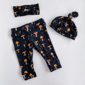 May include: A black headband with a bow, black leggings with a mushroom print, and a black beanie with a knot on top. The mushroom print features red, yellow, and white mushrooms.