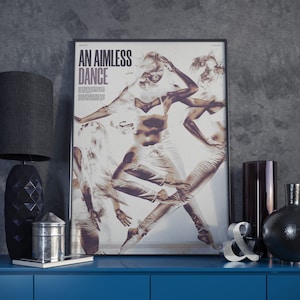 Puede incluir: Un póster enmarcado con el texto "AN AIMLESS DANCE" en letras negras sobre un fondo blanco. El póster presenta una imagen sepia de tres bailarines en el aire, con sus cuerpos superpuestos y creando una sensación de movimiento.