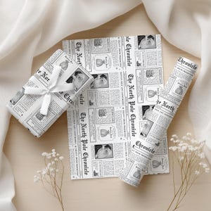 Pu&ograve; includere: Carta da regalo a tema natalizio e regalo confezionato con un nastro bianco. La carta presenta una stampa di giornale con il titolo "The North Pole Chronicle" e immagini di Babbo Natale e ornamenti natalizi. Su una superficie di legno chiaro.