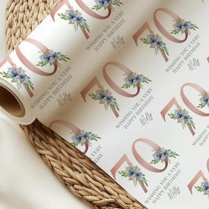 Op de afbeelding: Een rol wit cadeaupapier met een herhalend patroon. Het ontwerp toont het nummer 70 in roségoud, bloemaccenten en de tekst "Wishing you a very Happy Birthday Molly."