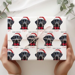 Può includere: Carta da regalo bianca con un motivo ripetuto di un Labrador nero con cappello da Babbo Natale e papillon rosso. Il nome "Cooper" e "Merry Christmas" sono stampati. Il regalo è legato con un fiocco di spago naturale.