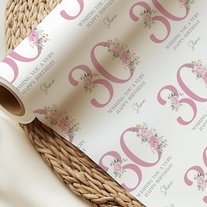 Può includere: Un rotolo di carta da regalo bianca con un motivo ripetuto del numero 30 in rosa, decorato con composizioni floreali. Il testo "Wishing you a very happy birthday" e il nome "Shona" sono anch'essi stampati.