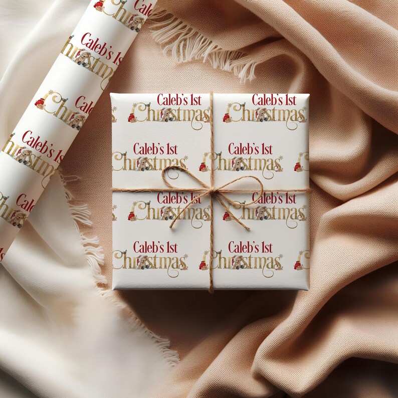May include: A wrapped gift and a roll of wrapping paper. The gift is wrapped in white paper with the text "Caleb's 1st Christmas" in gold and red. The gift is tied with twine. The wrapping paper has the same design.