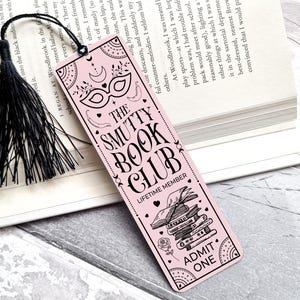 Puede incluir: Un marcap&aacute;ginas rosa con texto negro y una borla negra. El marcap&aacute;ginas presenta el texto "THE SMUTTY BOOK CLUB" e ilustraciones decorativas de una m&aacute;scara, libros y una rosa. Las palabras "ADMIT ONE" tambi&eacute;n est&aacute;n impresas.