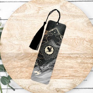 May include: Black and gold bookmark with a dragon silhouette and a celestial design. The bookmark has a black tassel.