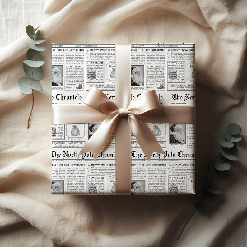 Pu&ograve; includere: Un regalo avvolto in carta da giornale con immagini di Babbo Natale e il testo "The North Pole Chronicle". &Egrave; legato con un nastro e un fiocco di raso color crema, su uno sfondo di tessuto neutro.