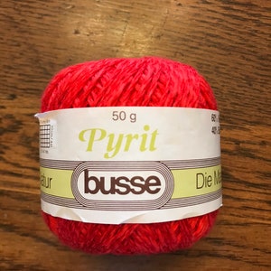 May include: A ball of red yarn labeled "Pyrit" with the brand name "busse" and the text "50 g" and "60% 40%"