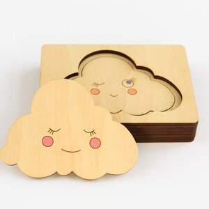 May include: A wooden puzzle featuring two clouds with smiling faces and closed eyes. The puzzle pieces are designed to fit together perfectly.