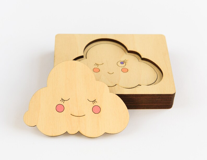 May include: A wooden puzzle featuring two clouds with smiling faces and closed eyes. The puzzle pieces are designed to fit together perfectly.
