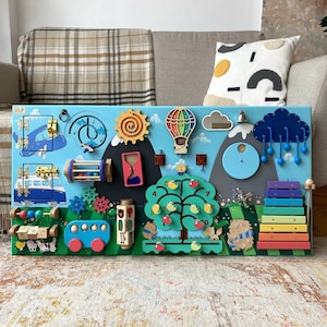 Puede incluir: Un tablero de actividades de madera colorido para niños pequeños con una variedad de características, que incluyen un autobús, un globo aerostático, una nube con lluvia, un xilófono, un árbol con manzanas, un juego de engranajes, una rueda giratoria y un laberinto de cuentas deslizantes.