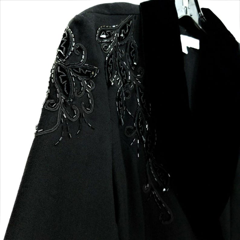 Puede incluir: Una chaqueta negra con cuello de terciopelo y adornos florales de cuentas en los hombros.
