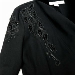 Puede incluir: Blazer negro con un dise&ntilde;o floral decorativo bordado en el hombro. El dise&ntilde;o presenta hojas de terciopelo negro y cuentas.